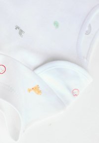 Dve biele bavlnené body s krátkymi rukávmi, zdobené viacfarebnými potlačami zvierat a červenými akcentmi na krku. Hladká, jemná textúra.