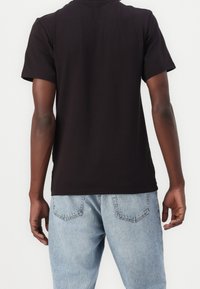 Zwarte katoenen T-shirt met korte mouwen, ronde hals, van achter gezien, gecombineerd met lichtblauwe denim jeans. Geen zichtbare patronen of logo's.