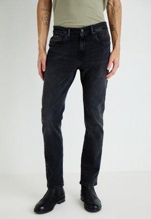 Jeans negri din denim cu o croială slim, cinci buzunare și detalii subtile de cusătură. Purtați cu o cămașă verde deschis și bocanci negri până la glezne.