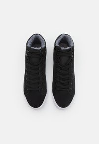 Zapatillas altas negras con una parte superior de tela texturizada y un forro suave gris, que cuentan con cordones negros y suelas de goma blancas.