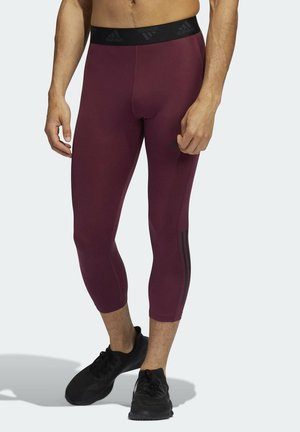 Collants de sport bordeaux avec une ceinture élastique noire portant le logo Adidas, de courte longueur avec des bandes noires sur les côtés.