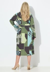 Sukienka z długim rękawem w zielone, czarne i niebieskie wzory z motywami roślinnymi; posiada pasek w talii i długość do połowy łydki. Gładka faktura tkaniny.