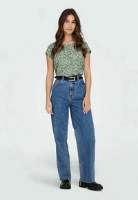 Green floral-patterned short-sleeve top paired with high-waisted blue denim jeans and a black belt, completed with black footwear.