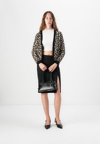 Kardigan dengan motif macan tutul, atasan cropped putih, rok pensil hitam dengan belahan, tas tangan hitam, dan sepatu hak runcing hitam. Desain simpel, bahan dengan tekstur.