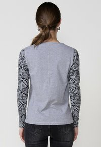 Camisa gris de manga larga con mangas negras estampadas, con un cuello redondo y un detalle de costura en la parte posterior. Tejido suave y con un ajuste casual.