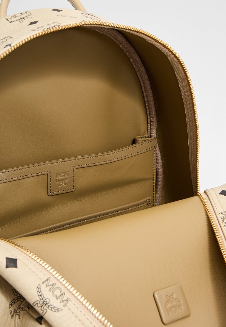 Beige Leder-Rucksack-Innenraum mit glatter Textur, Reißverschlusstasche, Logo-Patch und gemustertem Design auf dem Stofffutter.