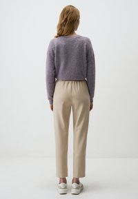 Maglione viola morbido e pantaloni beige a gamba affusolata con vita elastica, abbinati a sneakers bianche. Design semplice e texture morbide.