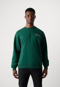 Sweatshirt en coton vert à manches longues et à col rond. Il présente l'inscription "Société du Café Paresseux" brodée en orange sur la poitrine.