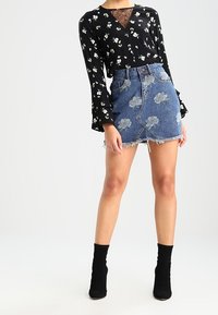 Blusa nera floreale con maniche lunghe, scollatura in pizzo a strati, abbinata a una mini gonna di jeans con orlo sfilacciato e fiori ricamati. Stivaletti neri alla caviglia.