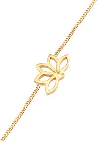 Bracciale in oro con un design floreale e dettagli intagliati, collegato a una catena fine. Il fermo è integrato nel design.