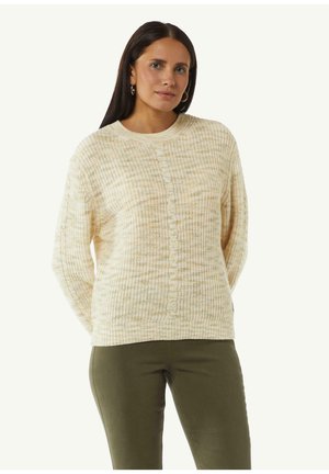 Sweter dziergany w kolorze kremowym z delikatnym wzorem w kratkę, okrągłym dekoltem, detalami z guzikami na środku i luźnym krojem. Spodnie w kolorze oliwkowym.