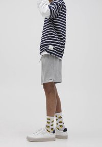 T-shirt rayé oversized bleu marine et blanc, shorts gris, baskets blanches et chaussettes jaunes à motifs, le tout sur un fond neutre.