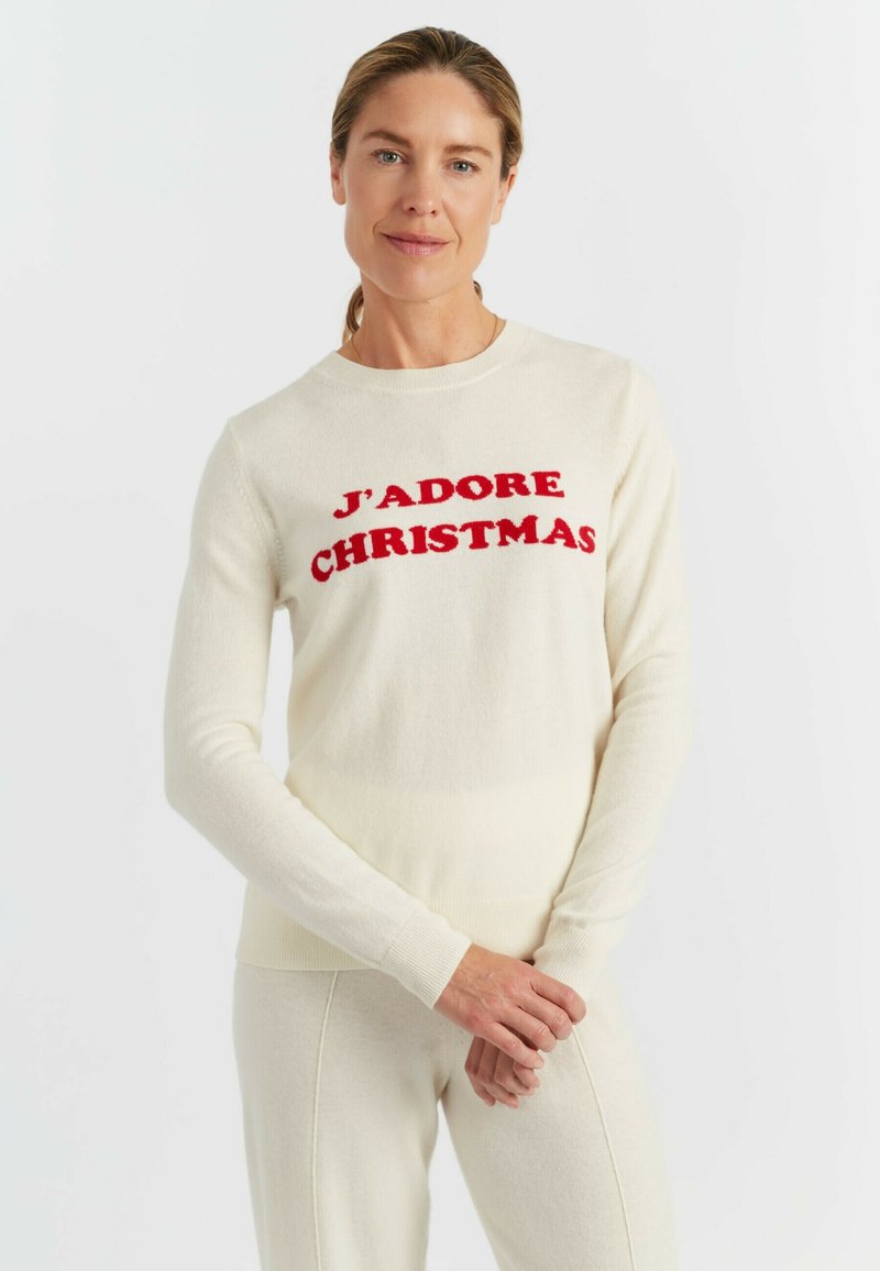 Crèmekleurige trui van zachte stof, met bold rode tekst "J'ADORE CHRISTMAS" op de voorkant; lange mouwen en een ronde halsdesign.