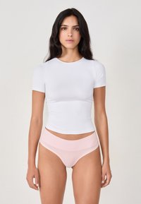Top corto bianco a maniche corte con design aderente, abbinato a biancheria intima alta di colore rosa chiaro con fascia liscia in vita e bordi senza cuciture.