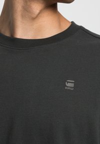 Czarna bawełniana koszulka z okrągłym dekoltem. Posiada małe szare logo z napisem "RAW" na lewej piersi. Miękka tekstura i regularny krój.