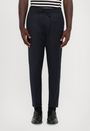 Navy jogger pants with an elastic waistband and drawstring, featuring a tapered fit. Material appears smooth with a subtle sheen.