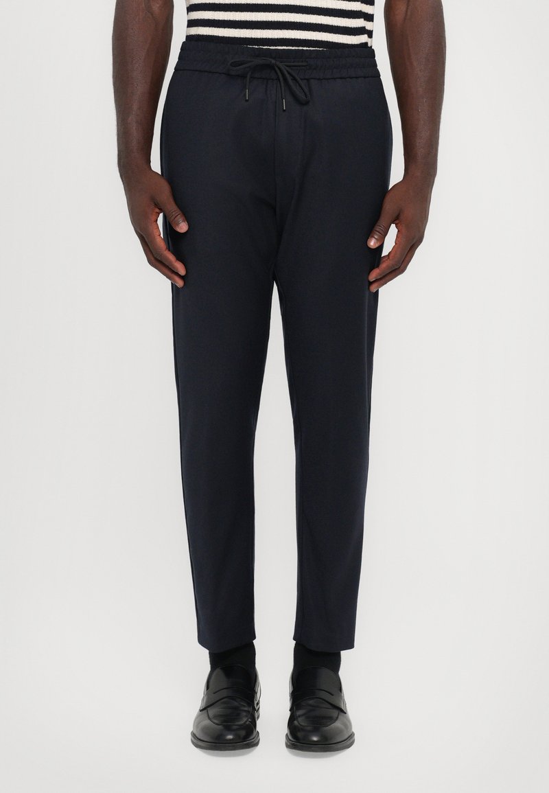 Pantalones jogger de color navy con cintura elástica y cordón, que presentan un ajuste ajustado. El material parece suave con un ligero brillo.