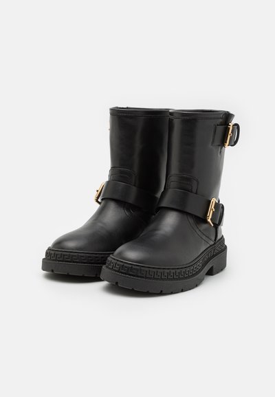 Bottines en cuir noir avec un bout arrondi, accents en métal doré, et une semelle extérieure épaisse texturée avec un bord à motif.
