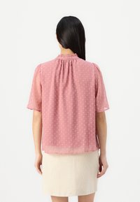Hellrosa Bluse mit kurzen Ärmeln, punktierter Textur, gerafftem Schnitt am Ausschnitt und lockerem Sitz, kombiniert mit einem cremefarbenen, strukturierten Rock.