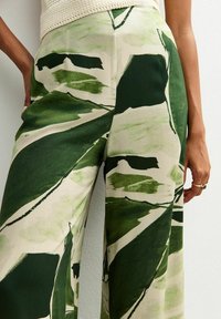 Brede broek met een bloemenpatroon in groen tinten op een crèmekleurige achtergrond. Gemaakt van lichte stof met een zachte textuur.