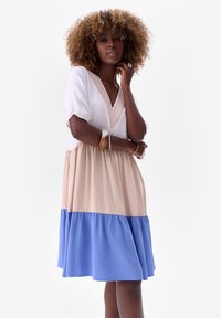 Kleurgeblokte jurk in wit, blush en blauw. Heeft een V-hals met borduursel en korte pofmouwen. Zachte stof, vloeiende silhoeet.