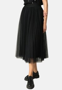 Jupe midi en tulle noir avec un design plissé et une taille élastique, associée à des chaussures noires à lacets.