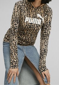 Sudadera con capucha de manga larga con patrón marrón y negro, que presenta un logo blanco de "PUMA". Combinada con una falda vaquera azul claro con una abertura lateral.