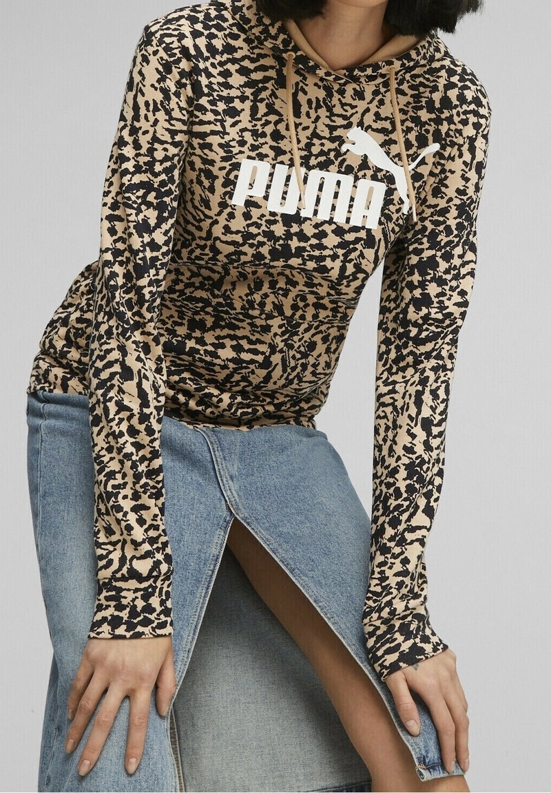 Sudadera con capucha de manga larga con patrón marrón y negro, que presenta un logo blanco de "PUMA". Combinada con una falda vaquera azul claro con una abertura lateral.