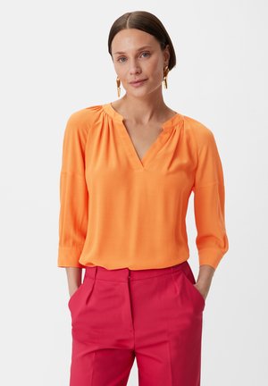 Orange blouse with a V-neckline and three-quarter sleeves. Made of lightweight fabric, featuring pleats at the shoulders.