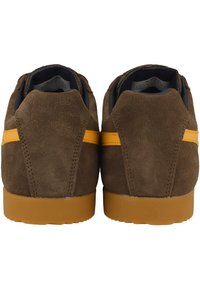 Ruskeat mokkanahka sneakersit, joissa on teksturoitu pinta, erottuva keltainen raita ja kumipohja. Sisältää pyöristetyn takakappaleen ja pehmustetun kaula-aukon mukavuutta varten.