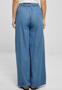 Denim byxor med vid ben, som har en avslappnad passform, något elastisk midjeband och en ljusblå färg. Tyget verkar mjukt med en subtil glans.