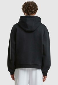 Sudadera negra con capucha y corte relajado, que presenta un bolsillo canguro, puños de canalé y una textura suave. La vista trasera muestra la capucha.
