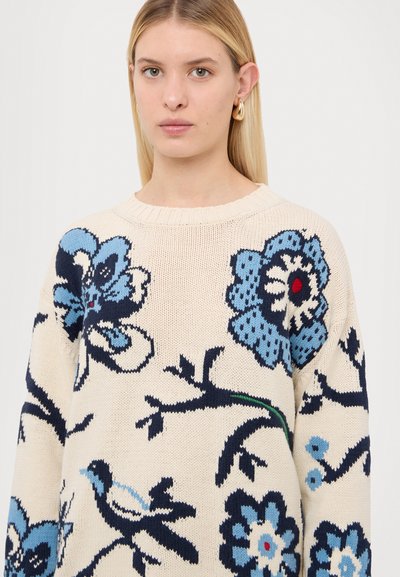 Suéter de punto con una base color crema y diseños florales azules, acentos negros y un cuello de canalé. Textura suave y corte relajado.