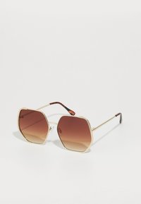Ochelari de soare hexagonali aurii cu lentile maro în degrade, cadru din metal, detalii texturate pe sprânceană și brațe cu model țestoasă.
