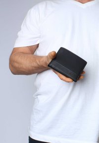 Black leather wallet held in a hand, featuring a smooth texture, a folded design, and minimalistic detailing with a logo embossed on the front.