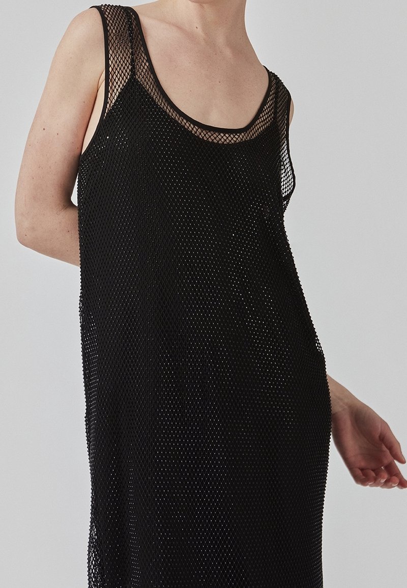 Débardeur en maille noire avec encolure dégagée, sans manches et structure ouverte, mettant en valeur une coupe ample et fluide.