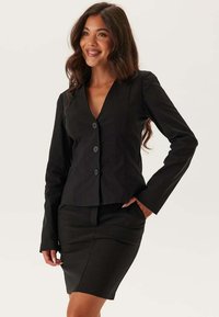 Svart figursydd kavaj med V-ringning och tre knäppningar, i kombination med en matchande pennkjol. Slät tyg och skräddarsydd design.