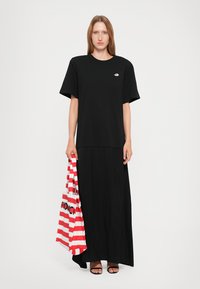 Black T-shirt dress with short sleeves, a relaxed fit. Accompanied by a red and white striped tote bag with black lettering. Smooth texture.