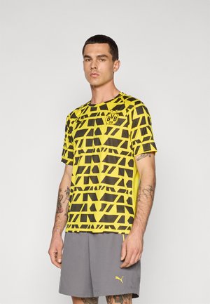 Tricou cu dungă galbenă și neagră, cu mâneci scurte, logo pe piept, asortat cu pantaloni scurți gri, cu un logo mic.