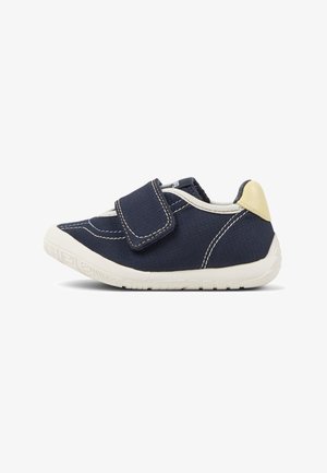 Scarpa in tessuto blu navy con chiusura a strappo in Velcro, suola in gomma bianca, parte superiore testurizzata e dettaglio beige sul tallone. Presenta cuciture visibili.
