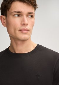 Schwarzer Sweatshirt mit Rundhalsausschnitt, gerippten Bündchen, weicher Textur und einem dezenten gestickten Logo auf der Brust.