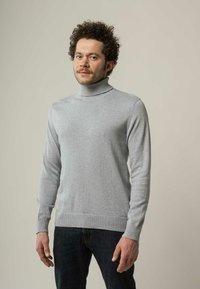 Grauer Rollkragenpullover aus weichem Material, mit langen Ärmeln und geripptem Struktur an den Bündchen und am Saum, kombiniert mit dunklen Jeans.