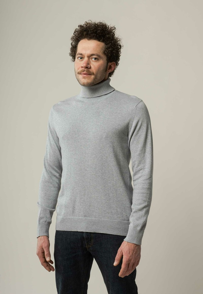 Grauer Rollkragenpullover aus weichem Material, mit langen Ärmeln und geripptem Struktur an den Bündchen und am Saum, kombiniert mit dunklen Jeans.