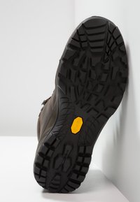 Brun tursko med dype spor slik som på sålen, svart gummimateriale og med en gul Vibram-logo. Designet har hevede mønstre.