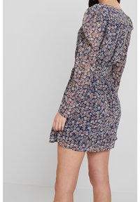 Vestido floral con un fondo azul oscuro y pequeñas flores en tonos rosa y blanco, mangas largas, detalle de hombros fruncidos y una falda acampanada.