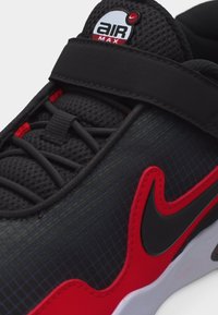 Κοντινή λήψη μαύρου και κόκκινου αθλητικού παπουτσιού Nike Air Max με υφή από δίχτυ, μαύρο λουράκι και μαύρο λογότυπο Swoosh με κόκκινο περίγραμμα σε λευκή σόλα.