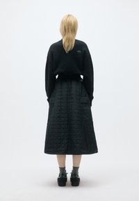 Sweatshirt de fleece preto, saia longa preta acolchoada e sapatos escuros. Design simples com uma superfície texturizada e cintura ajustada.