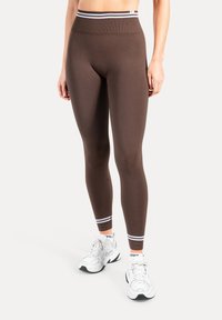 Leggings marron taille haute avec une texture lisse et des rayures horizontales contrastantes sur la taille. Assortis à des baskets blanches.