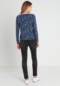 Maglietta a maniche lunghe di colore blu navy con un motivo floreale, abbinata a jeans skinny scuri e sneakers bianche. Il tessuto sembra morbido e liscio.