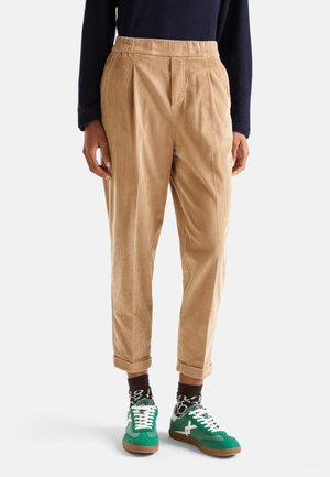 Persona che indossa pantaloni di velluto a coste beige con i risvolti, calze scure a fantasia, sneakers verdi e bianche e una maglia scura a maniche lunghe.